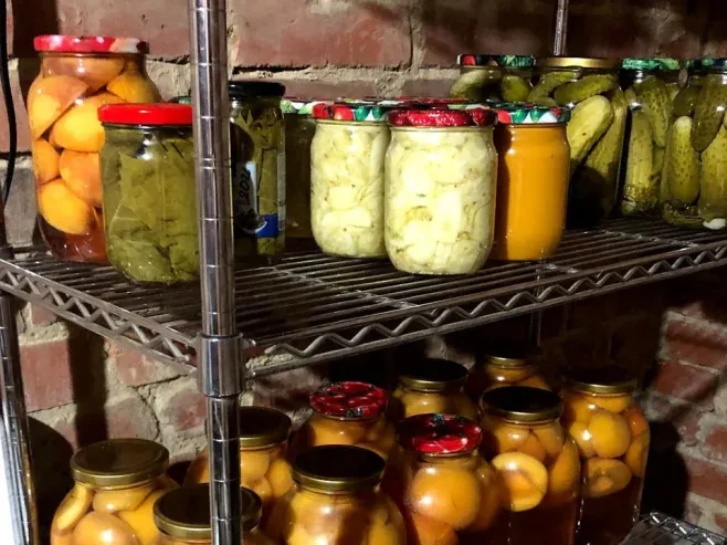 Банки з консервованими персиками, огірками та овочами на полицях
