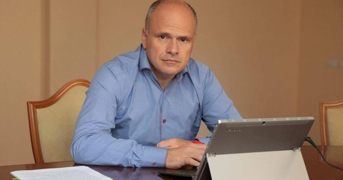 Чоловік у блакитній сорочці сидить за столом з ноутбуком і документами