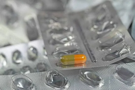 Помаранчево-жовта капсула на срібному блістері серед порожніх упаковок ліків